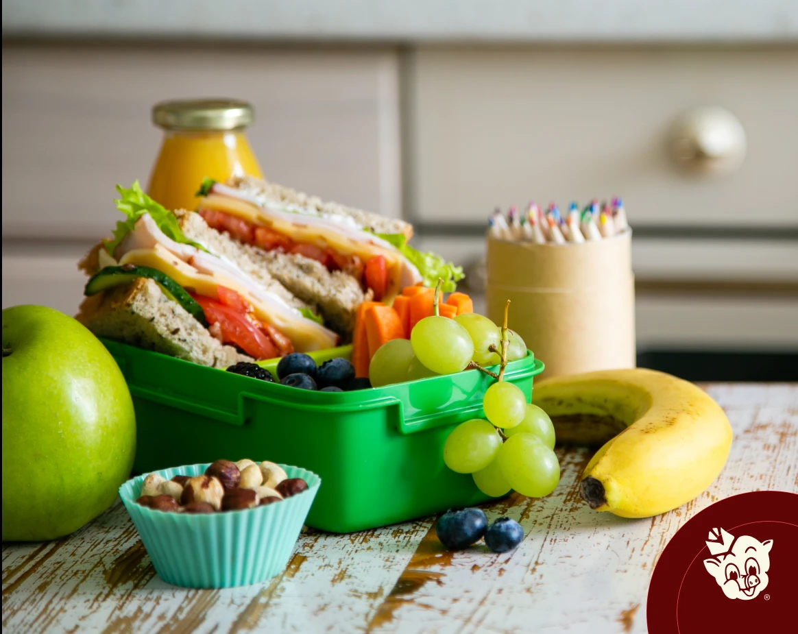 Healthy school lunchbox with a turkey and cheese sandwich, apple, banana, grapes, blueberries, carrots, mixed nuts, and juice, featuring fresh back-to-school grocery essentials from Russell's Piggly Wiggly.