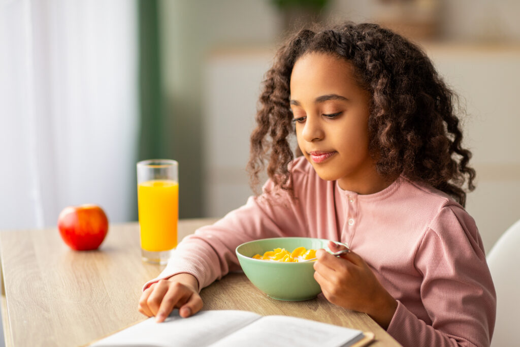 School-age child reading a book while eating a healthy breakfast with cereal, orange juice, and a fresh apple, highlighting back-to-school grocery essentials available at Russell's Piggly Wiggly.