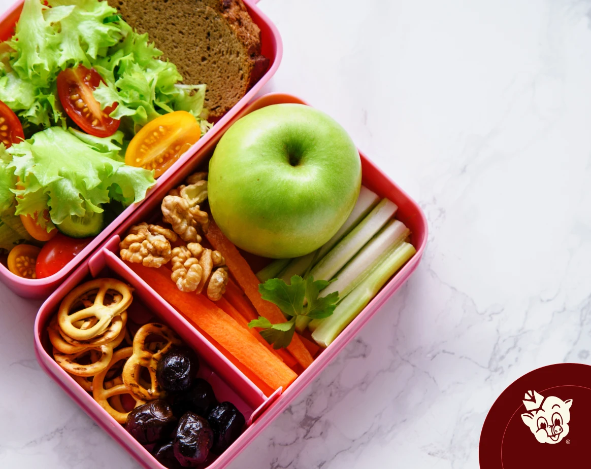 Healthy back-to-school lunchbox with fresh salad, green apple, carrot sticks, celery, walnuts, pretzels, olives, and whole grain bread, featuring nutritious meal ideas from Russell's Piggly Wiggly.