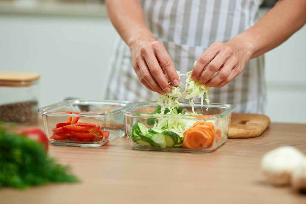 Preparing fresh vegetables for meal prep in reusable containers with cabbage, cucumbers, carrots, and bell peppers for easy summer-to-school meals from Russell's Piggly Wiggly.